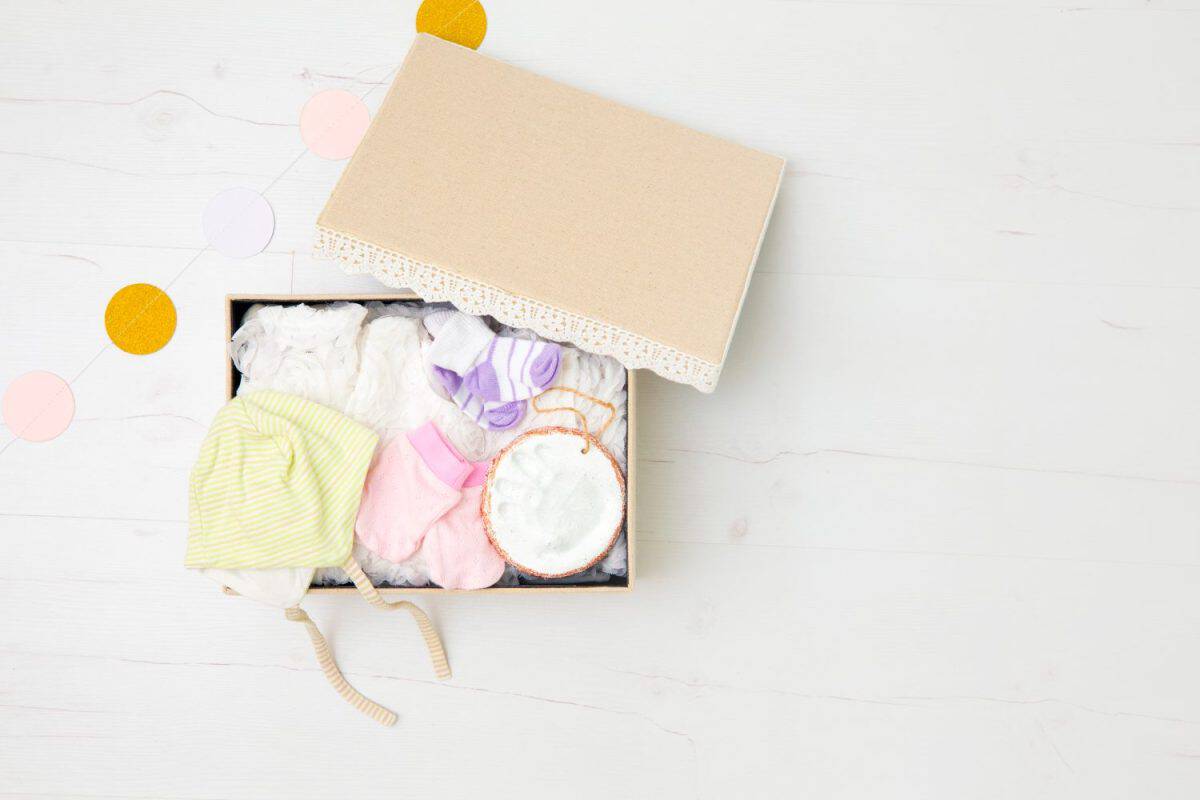 Vintage keepsake box for preserving baby`s first clothes and things concept. Newborn baby clothes in box hat, gloves, dress, socks, clay hand print to preserve mother`s and baby`s first memories.