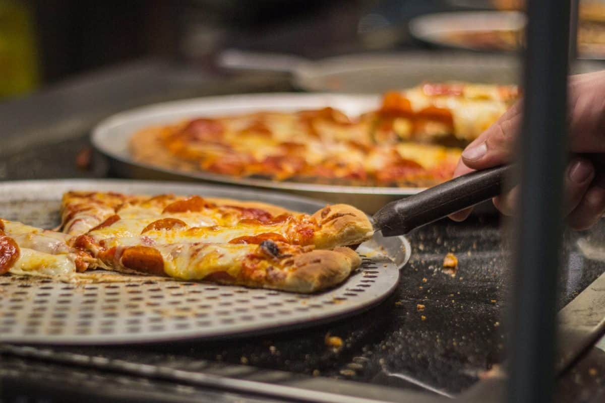 man's hand takes a slice of pizza on a buffet