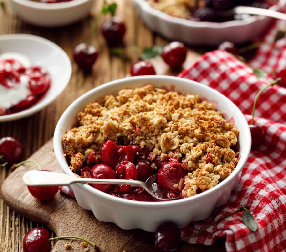 Cherry crumble, stewed fruits topped with crumble of oatmeal, almond flour, butter and sugar in a baking dish on a wooden table, close-up