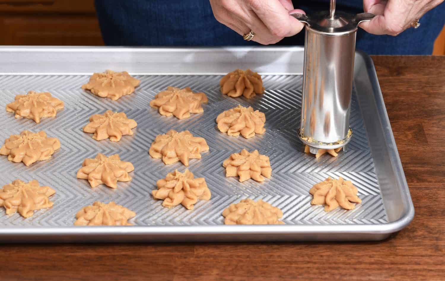 Closeup of a home baker using a cookie press to form cookies on a baking sheet.