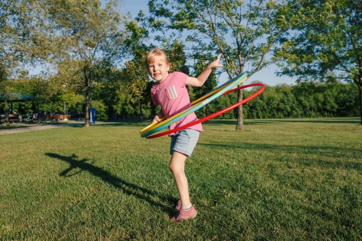 Cute smiling Caucasian preschool girl playing with hoola hoop in park outside. Kids sport activity. Lifestyle happy childhood. Summer seasonal outdoor game fun for kids children.