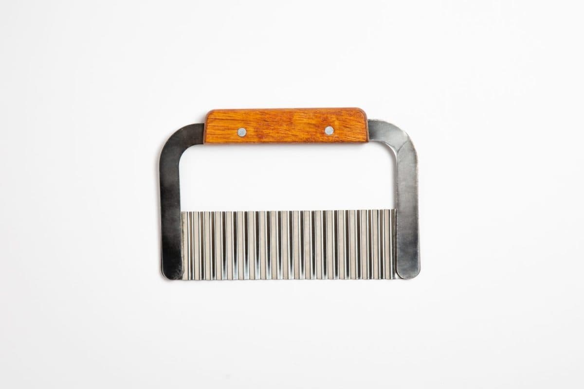 Close up of a hand crinkle cut potato chipper on white background.Stainless steel knife with a wooden handle for potatoes and carrots.High resolution photo.