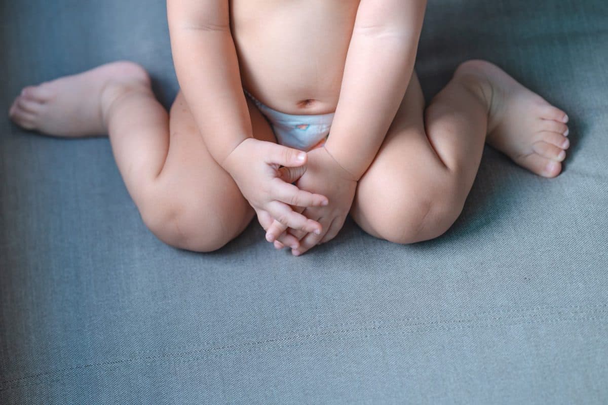 Little baby sitting W posture on the gray sofa,Which is called W-sitting knees bent and feet positioned outside hips can cause to hip dislocation.