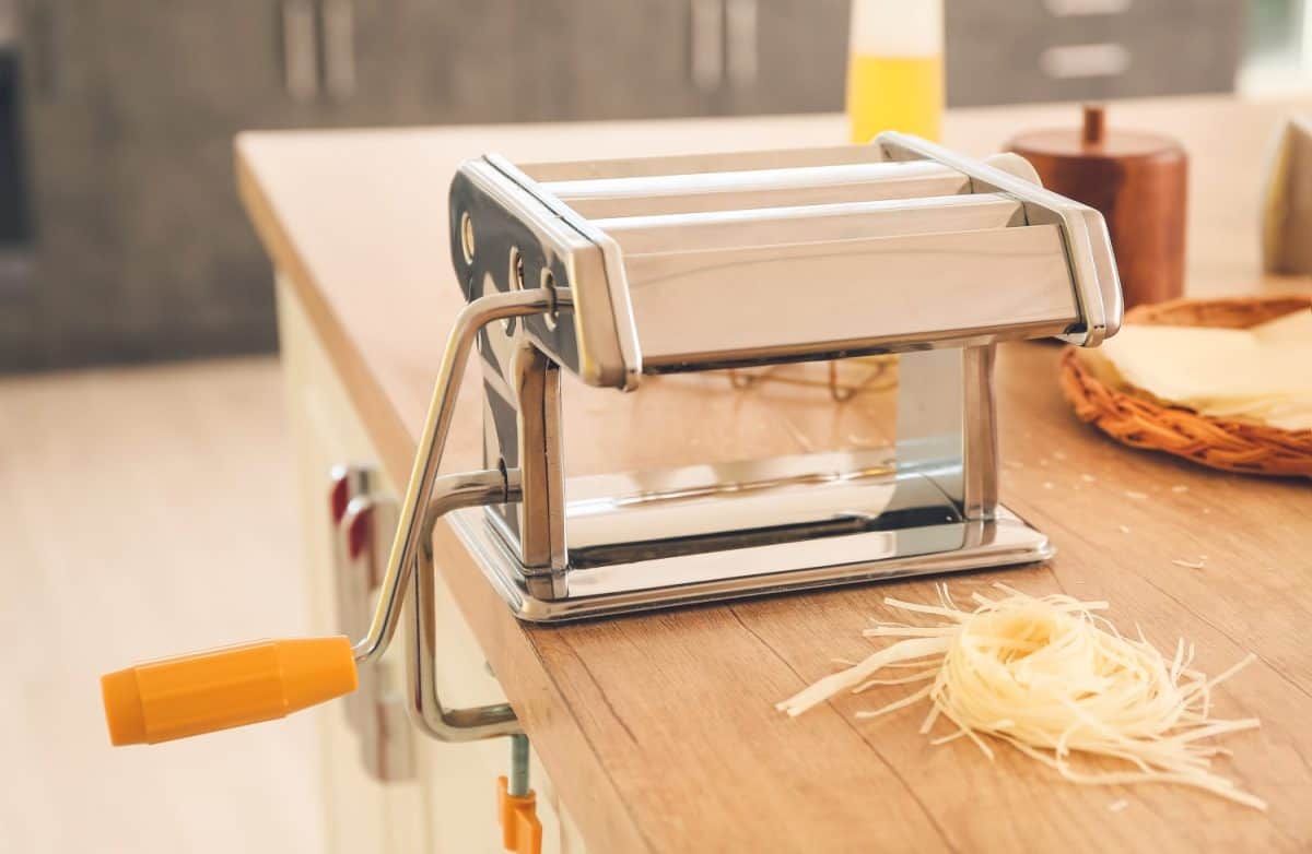 Pasta maker with dough on table in kitchen