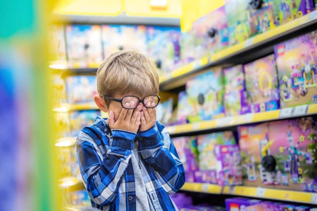 The little boy in the toy store is upset. The kid covered his eyes with his hands, crying. Child's tears in toy shop.