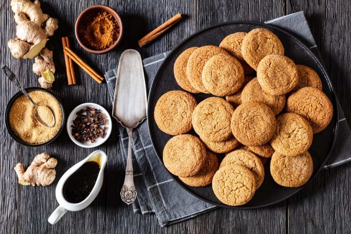 soft ginger cookies on black plate on dark oak table with ingredients, horizontal view from above, flat lay