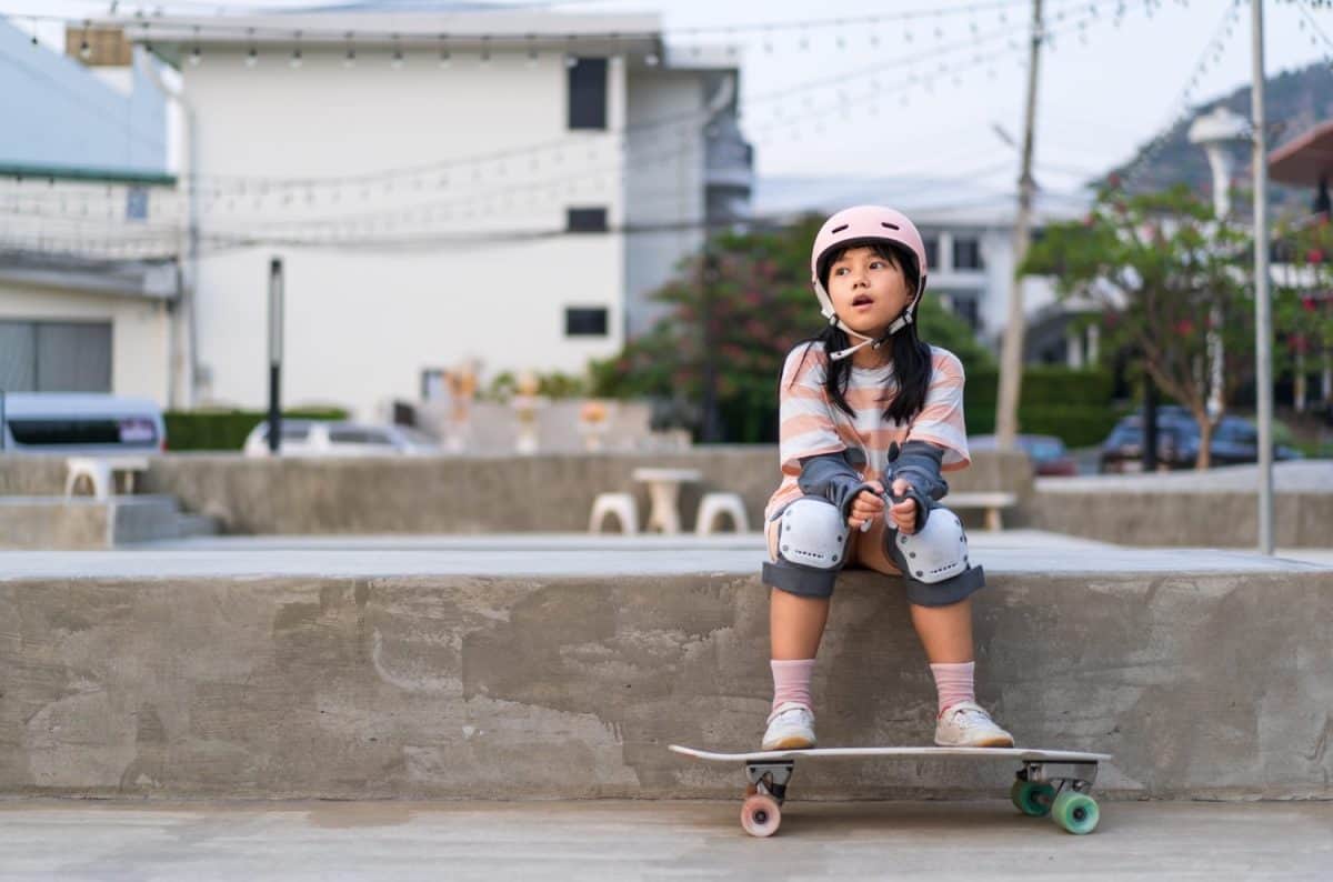 asian child skater or kid girl sitting relax at skatepark with skateboard or surf skate to people extreme sports in skate park by surfskate to wears helmet elbow wrist knee guard for body safety