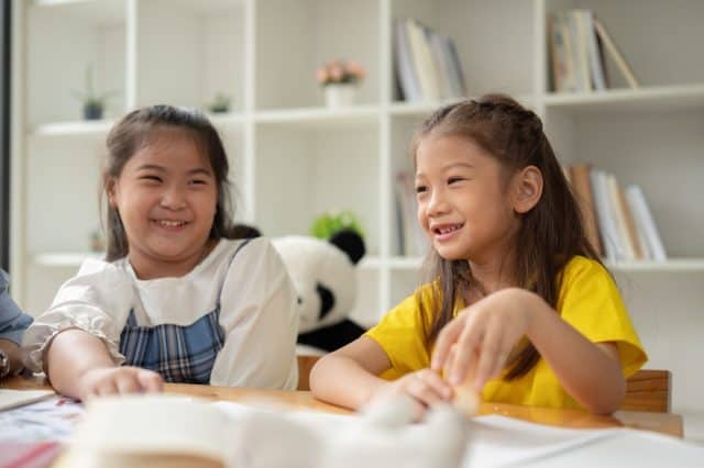 Two adorable young Asian girls are enjoying talking on a small break in a classroom together. children, kids, preschool, kindergarten students