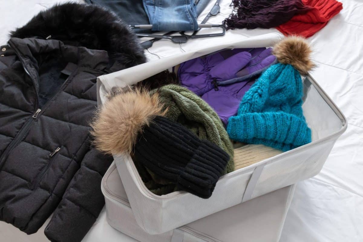 Horizontal photo, winter clothes on a bed, woolen hats and scarf, tucked in cloth boxes to be collected by the beginning of spring. Closet change.