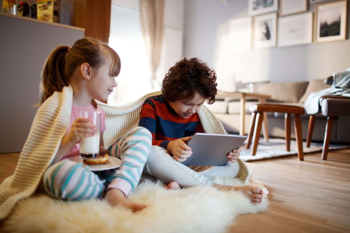 Little boy using tablet with his sister on living room floor