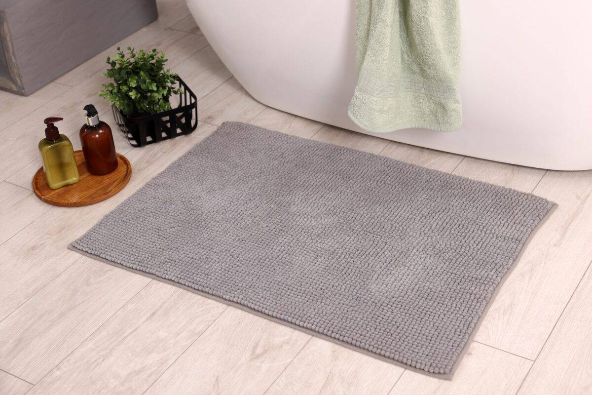 Soft bath mat, green plant and cosmetic products on floor in bathroom