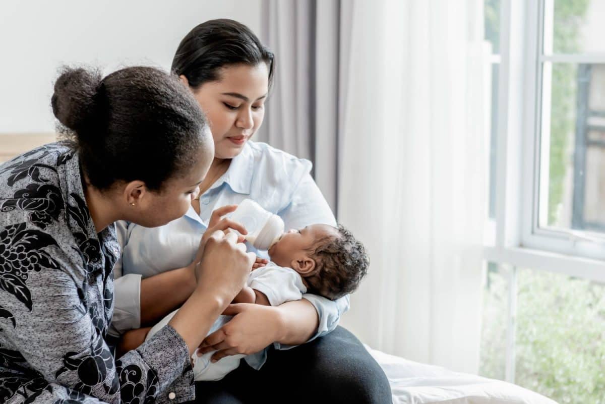 an African mother and babysitter feeding milk from bottle milk to her 2-month-old baby newborn son, to African family and food for infant concept.