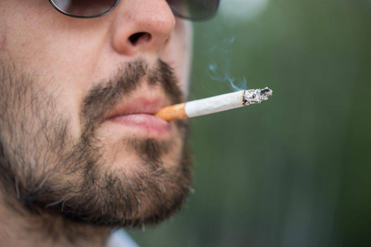 Close-up shot of bearded man in sunglasses smoking cigarette.