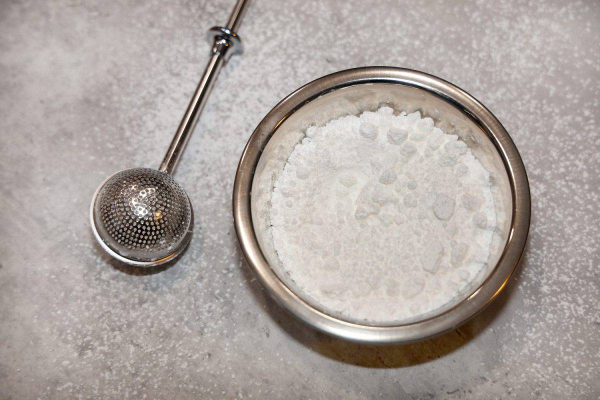 View of a small bowl of powdered sugar and a stainless steel sugar duster on the side.