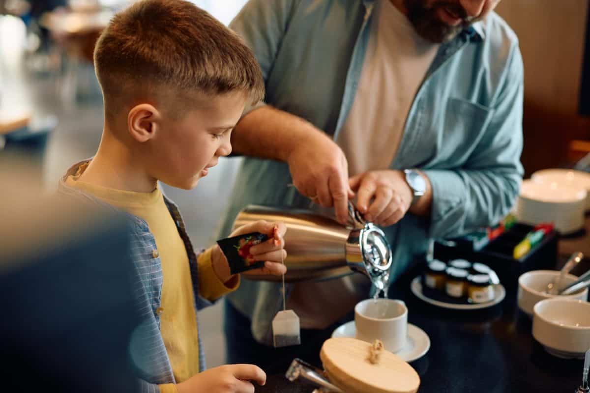 Smiling kid having cup of tea during buffet breakfast with his father in a hotel.