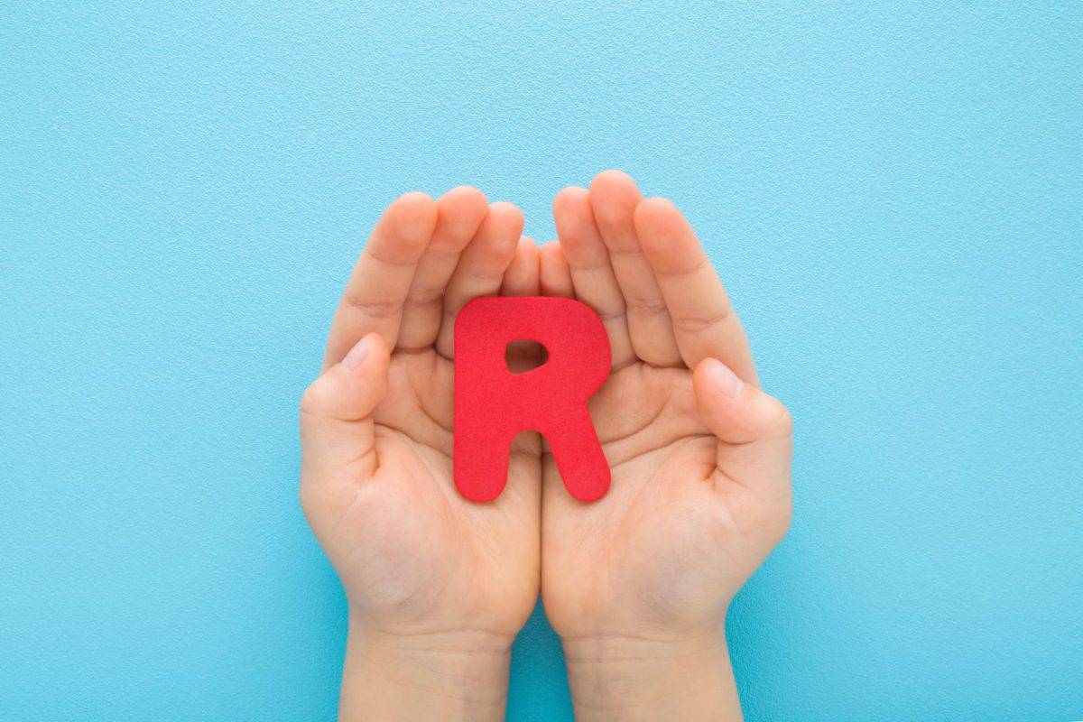 Baby boy hands holding red R letter on light blue table background. Pastel color. Time to learning. Closeup. Point of view shot.