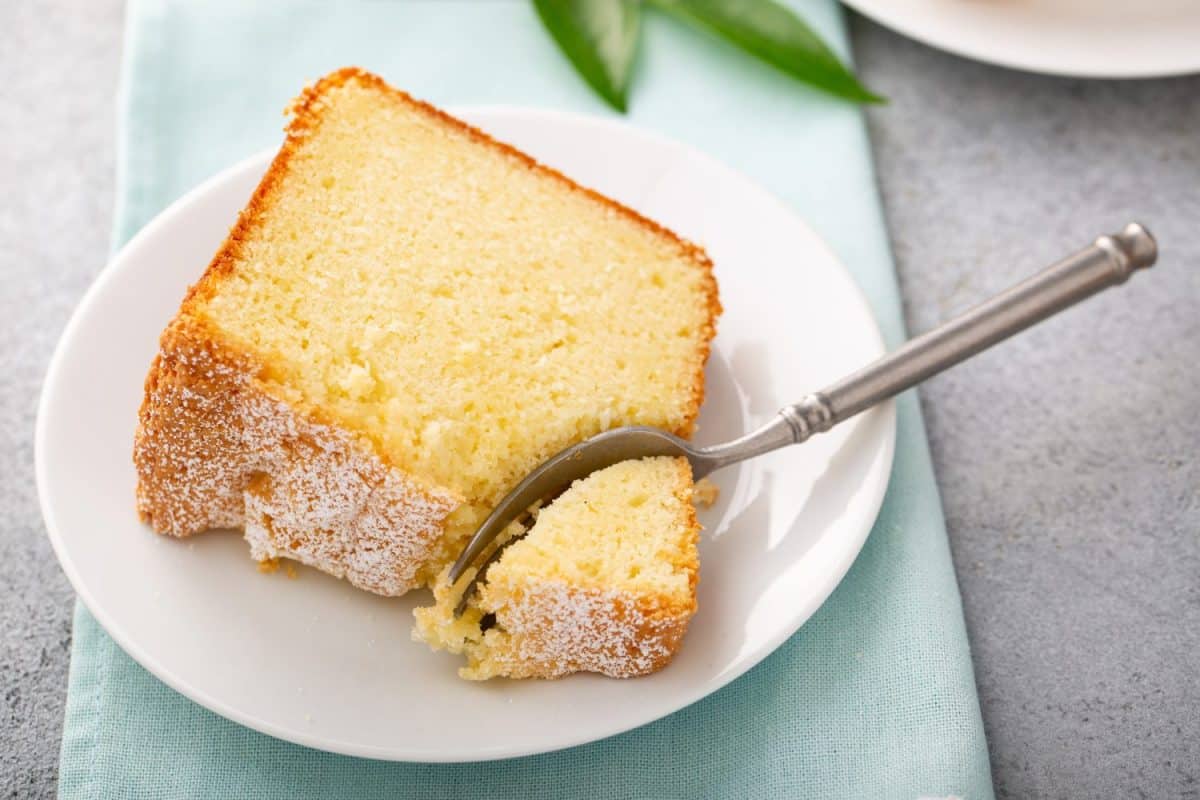 Lemon pound cake baked in a bundt pan sliced topped with powdered sugar, slice on a plate