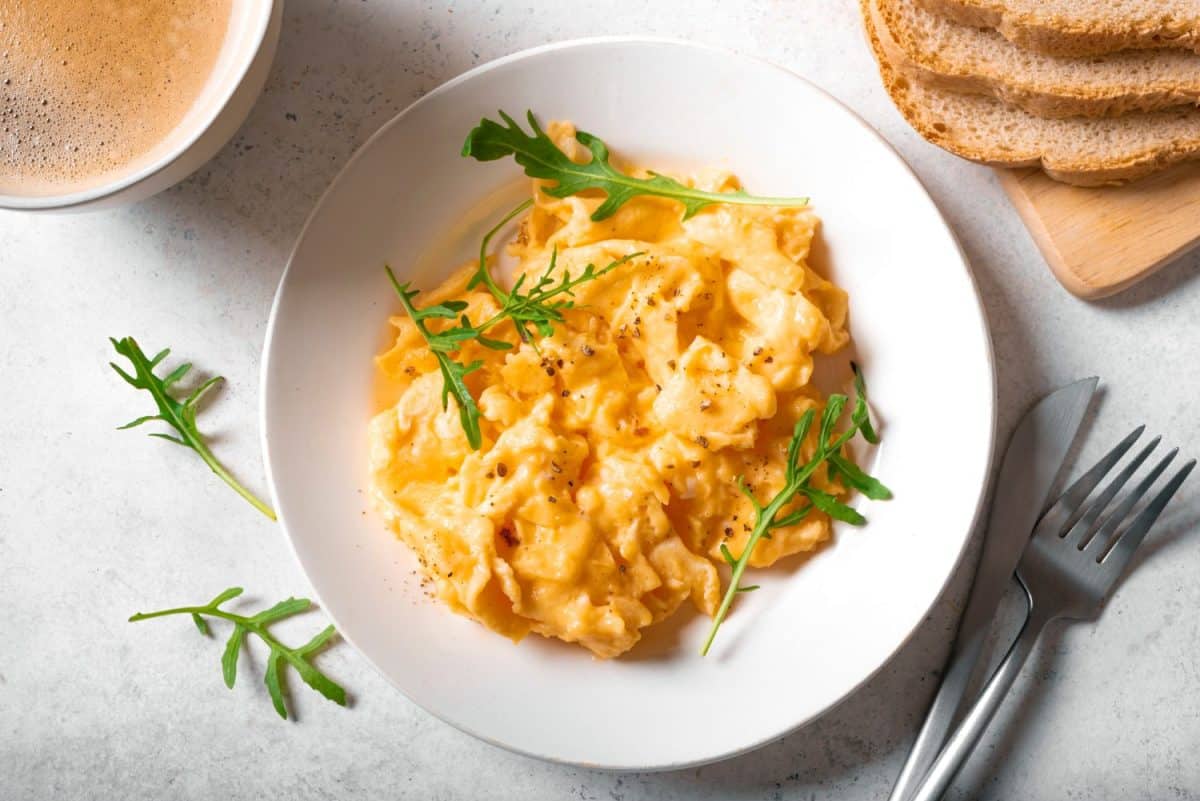 Scrambled eggs and cup of coffee for healthy breakfast on white background, top view. Fluffy scrambled eggs on white plate.