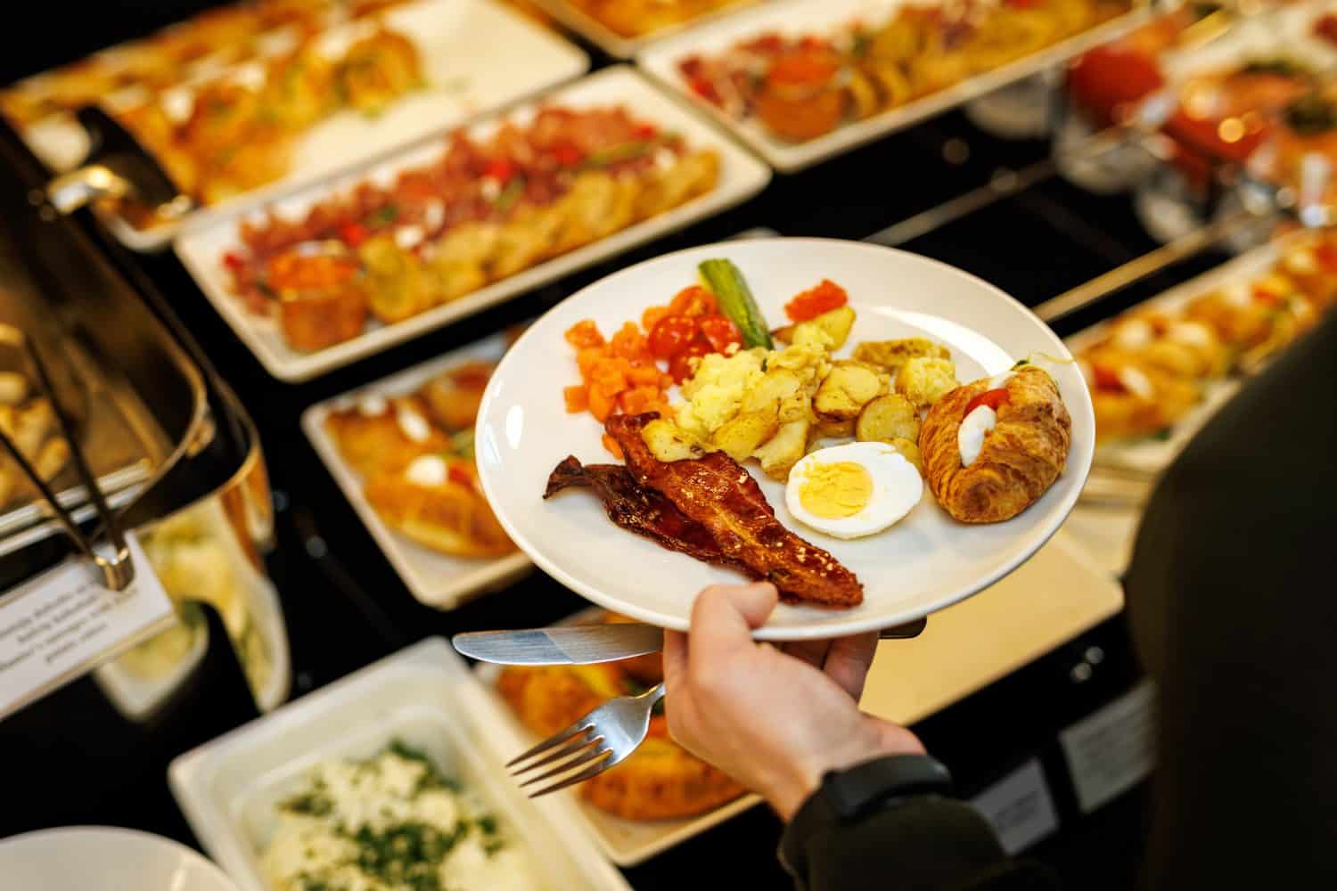 Guest picks up different food at the breakfast buffet at the hotel