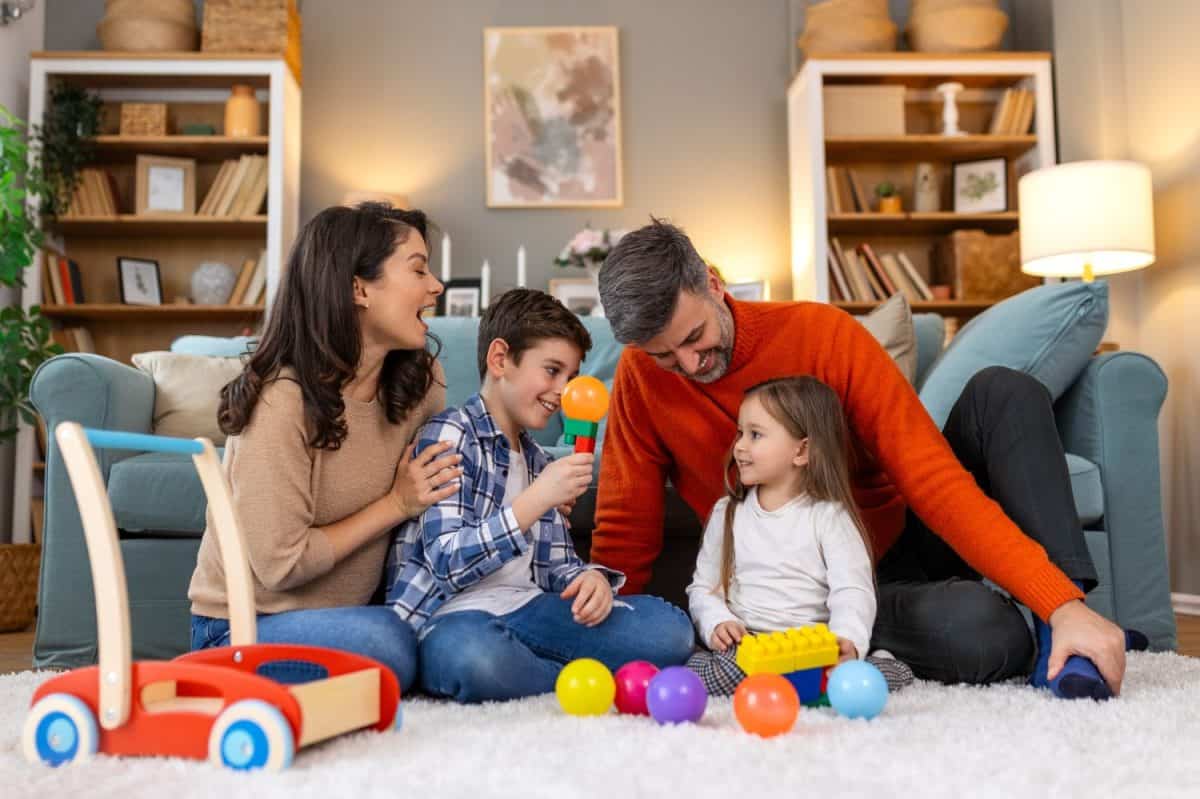 Happy family having fun with toys, parents and little children sit on sofa together, Happy family sitting on sofa playing together. Cheerful parents playing with their kids at home.