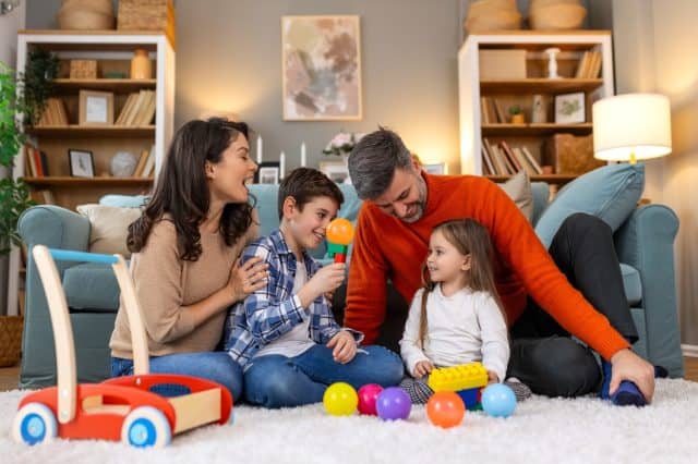 Happy family having fun with toys, parents and little children sit on sofa together, Happy family sitting on sofa playing together. Cheerful parents playing with their kids at home.