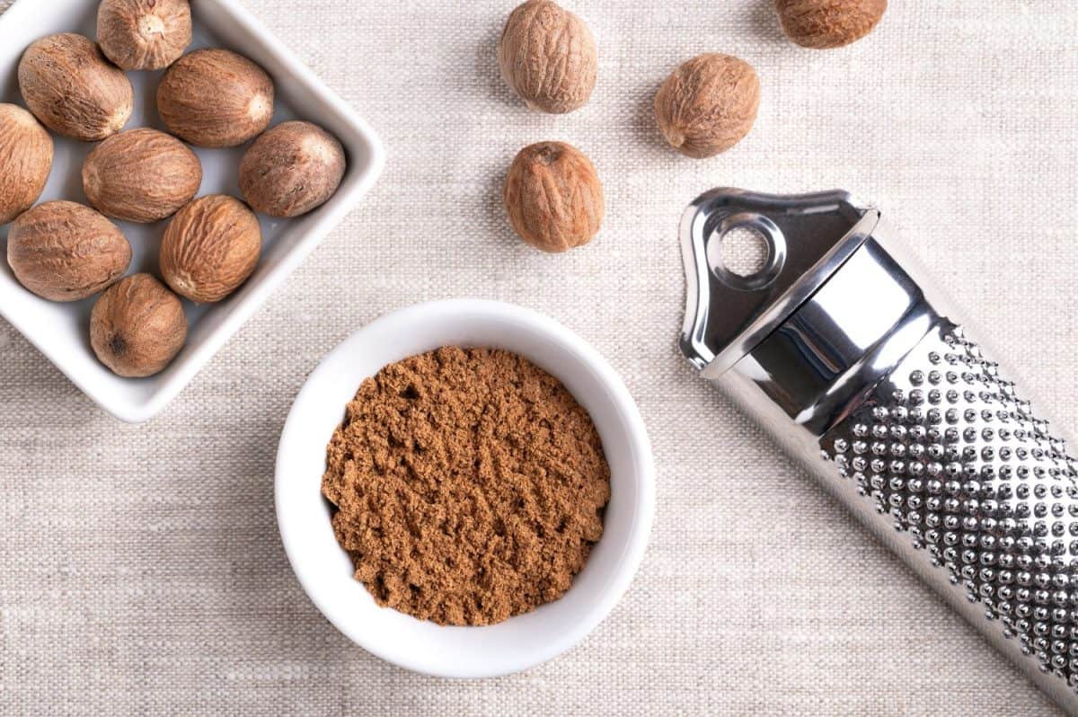 Nutmeg powder, ground nutmeg in a small white bowl on linen fabric. Fragrant or true nutmeg, a spice, also used in traditional medicine. With dried seeds of Myristica fragrans and a nutmeg grater.