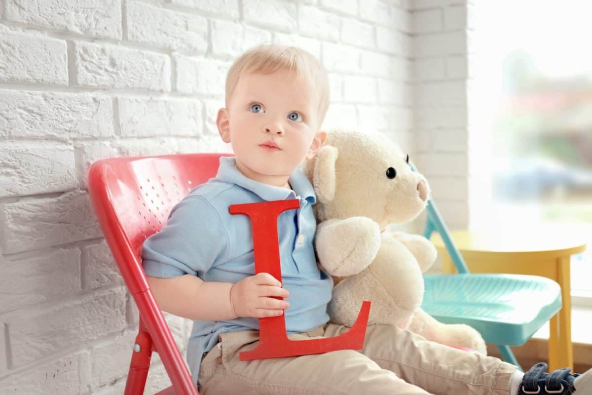 Cute little boy with letter L sitting on chair at home