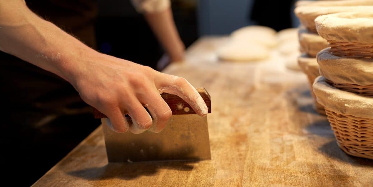 food cooking, baking and people concept - chef or baker portioning dough with bench cutter at bakery