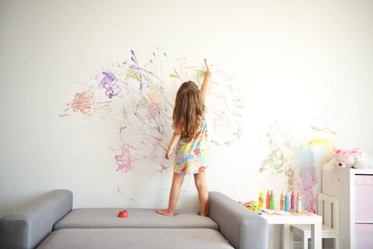 Curly cute little toddler girl painting with paints color and brush on the wall. Works of child