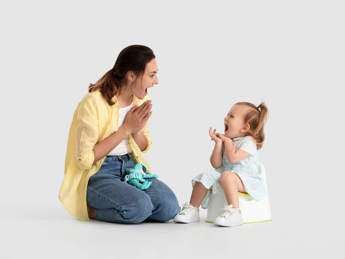 Mother potty training her little daughter on light background