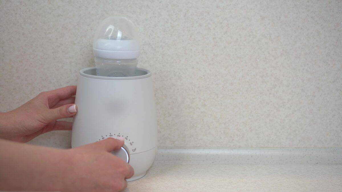 A woman puts a bottle of food into a bottle warmer. Apparatus for rapid heating and stirring of infant formula.