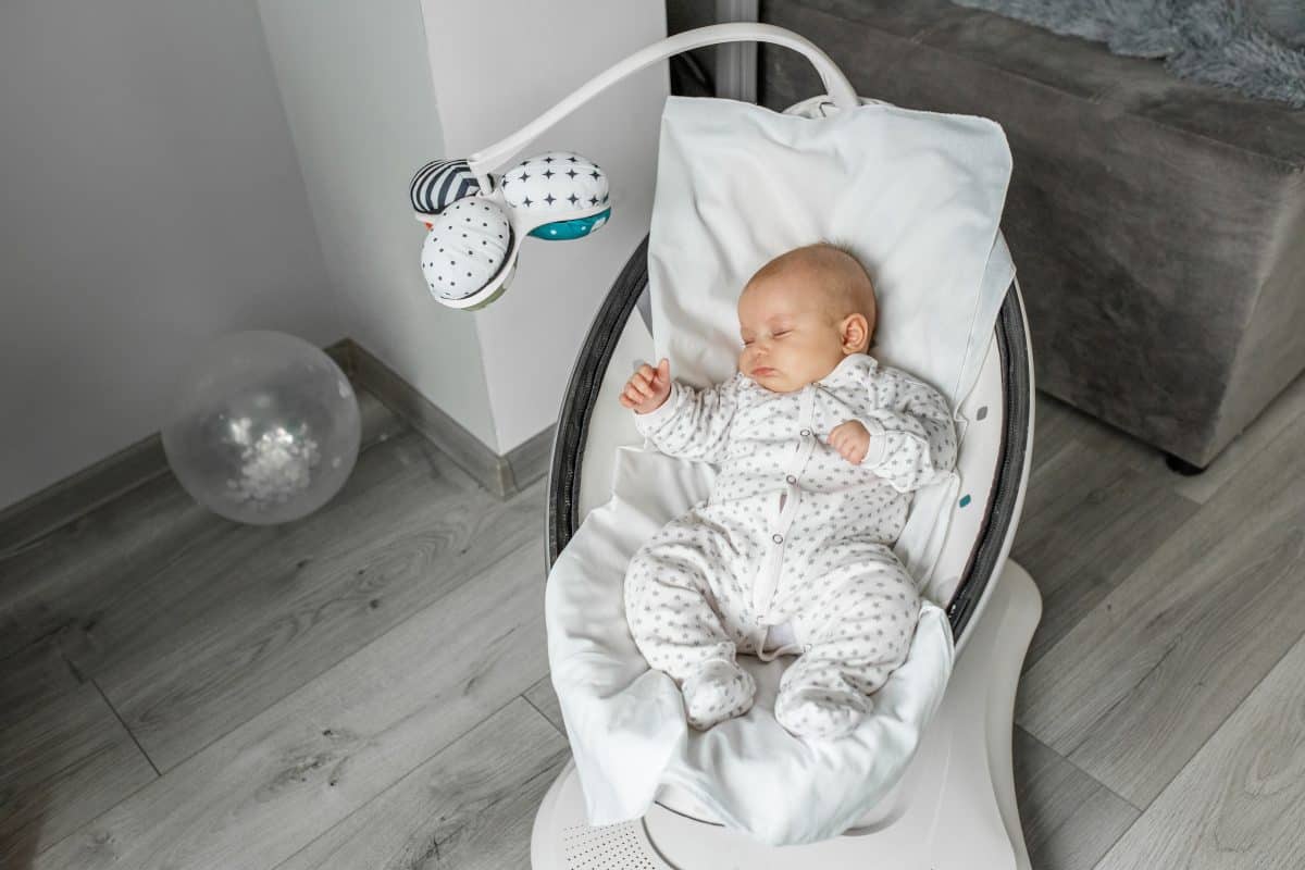 Adorable baby sleeps in baby swing in room. Newborn concept.