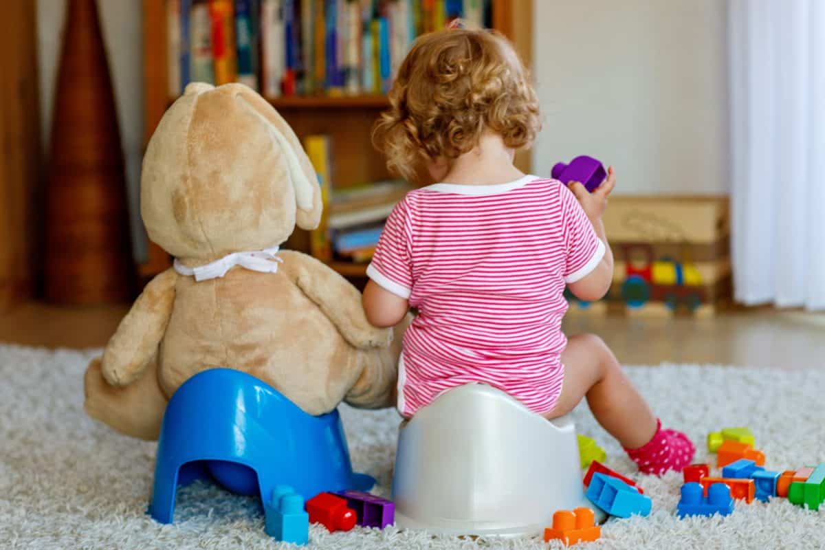 Closeup of cute little 12 months old toddler baby girl child sitting on potty. Kid playing with doll toy. Toilet training concept. Baby learning, development steps