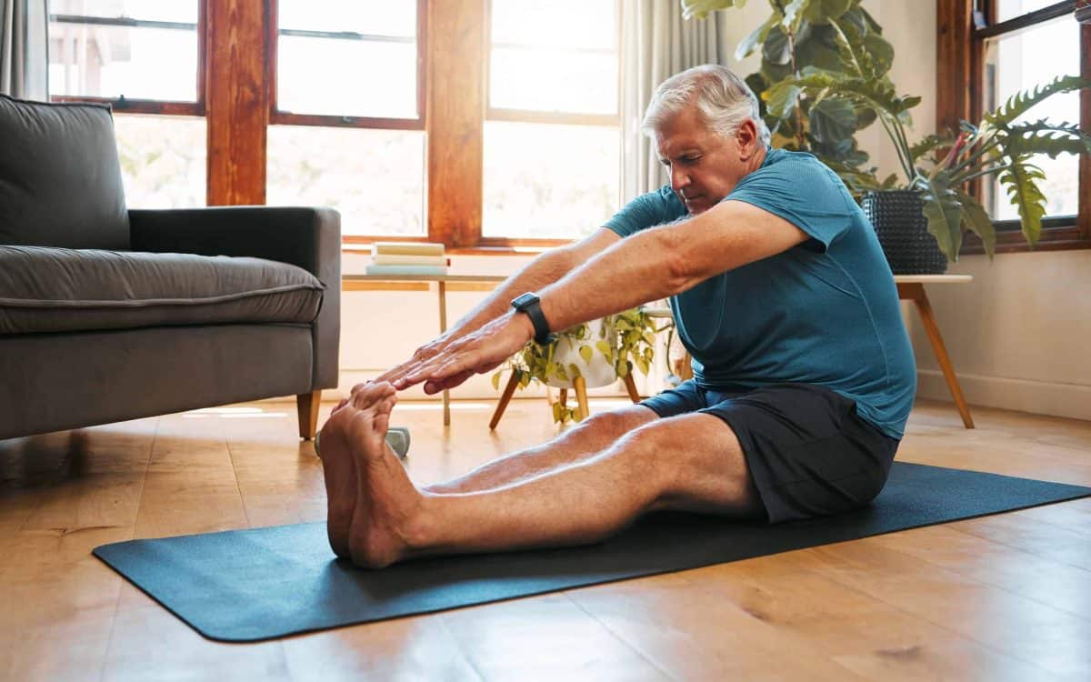 Health, exercise and yoga with senior man doing ground stretching before meditation and wellness workout. Fitness, relax and floor warm up by elderly male start healthy cardio training in living room