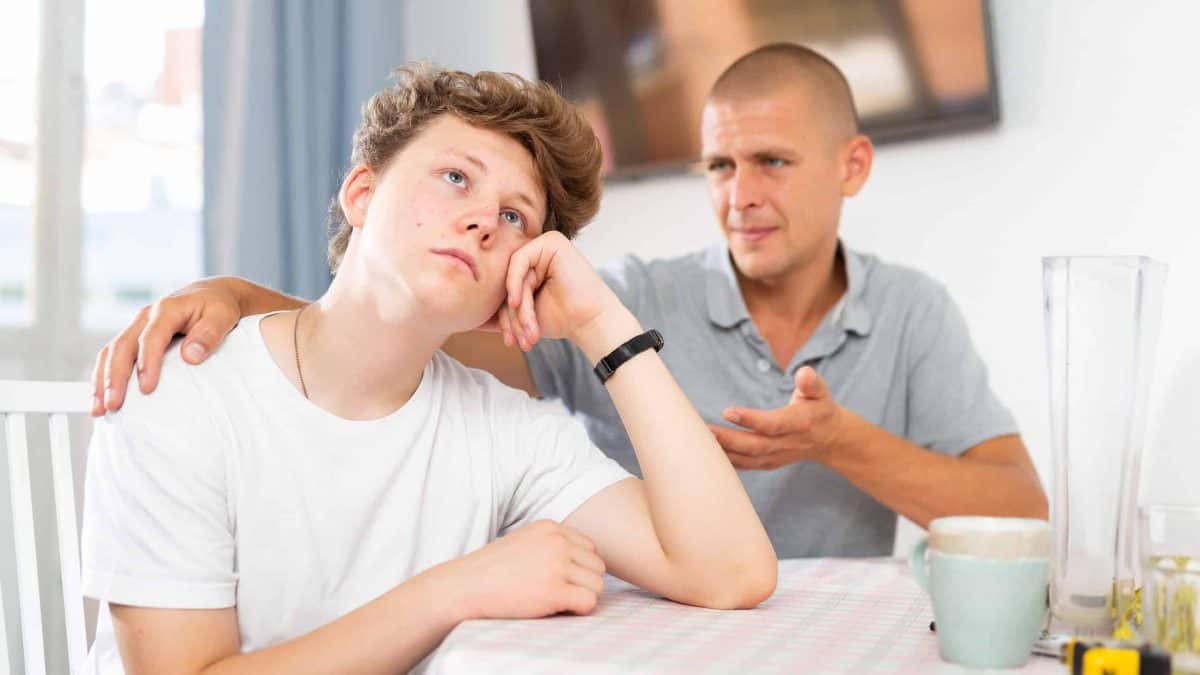 Teenager boy feeling upset. His father sitting next to him and comforting.