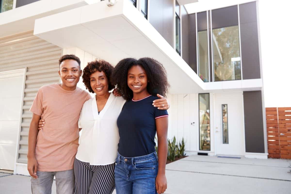 Black middle aged single mother and her kids standing in front of their modern home,close up