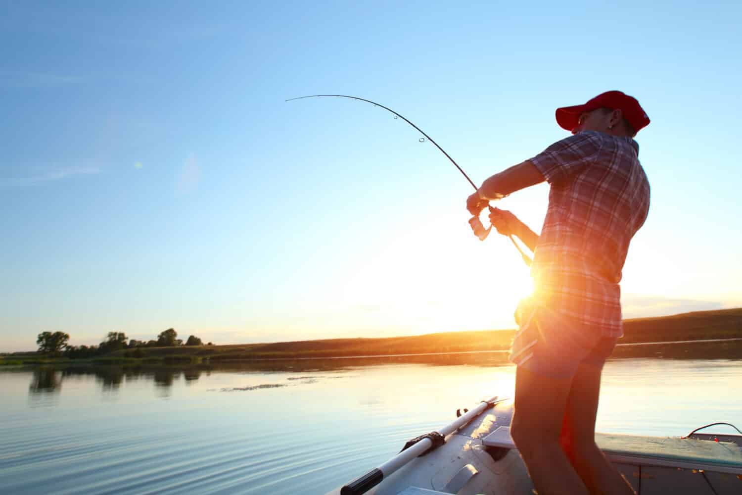 Young man fishing on a lake from the boat at sunset