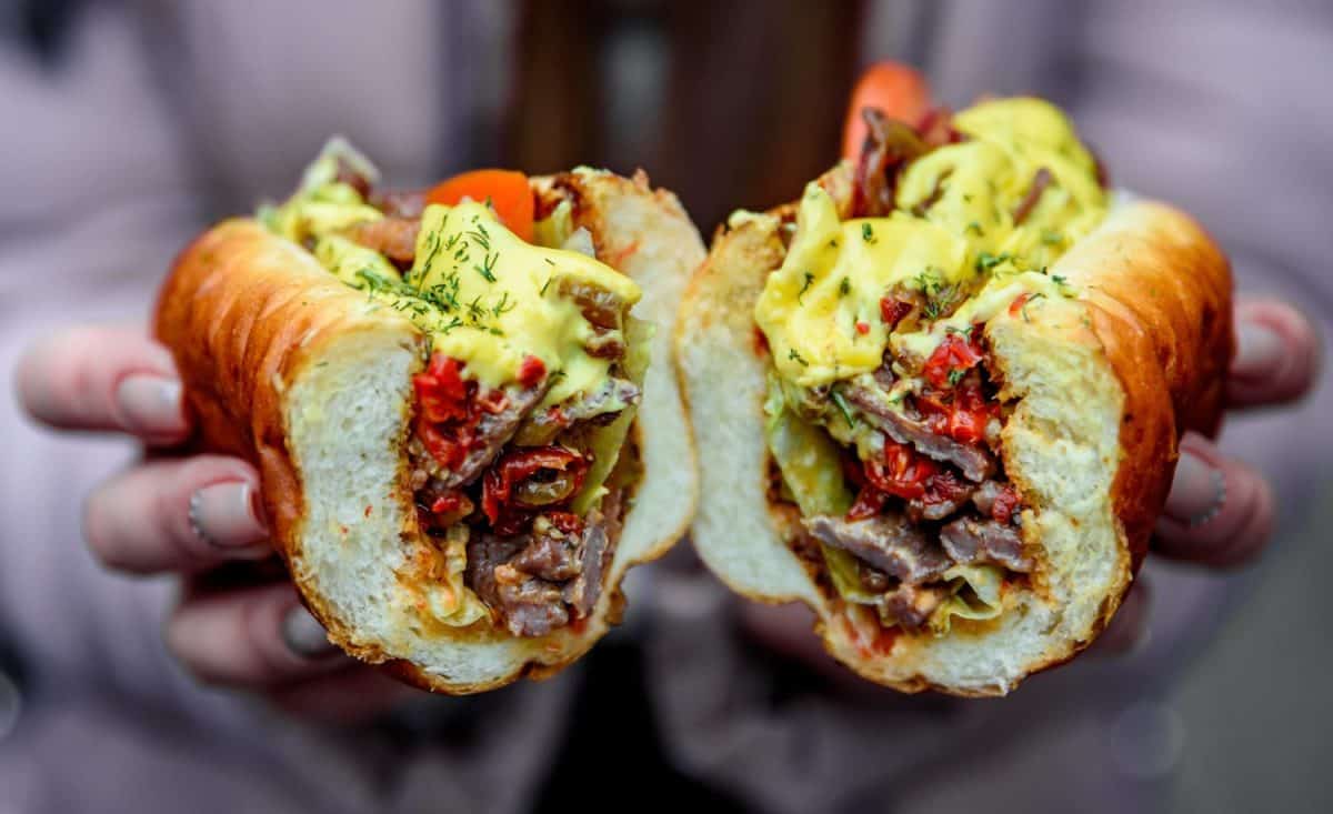 woman hand hold cut Philly cheese steak sandwich with meat, vegetables, cheese and sause