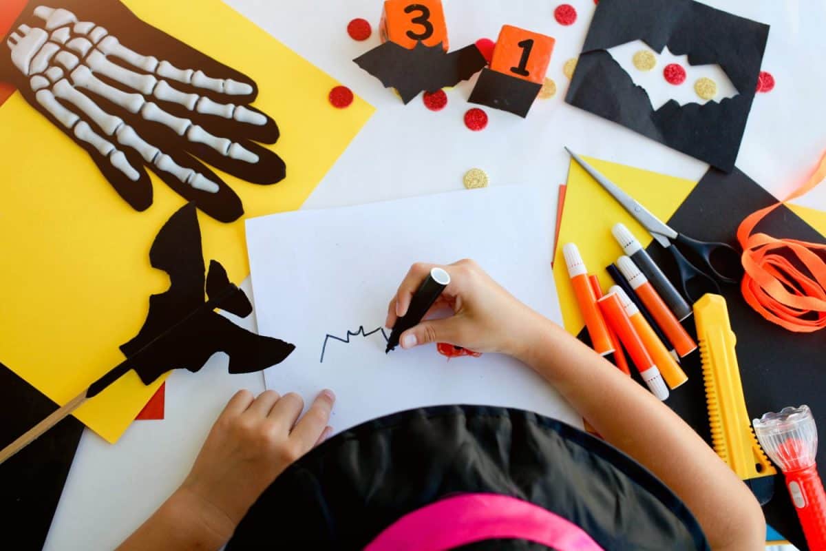 Little girl in a witch costume draw a bat, for the holiday of halloween on a light table. Halloween decor. Handicraft. The concept for Halloween. DIY.