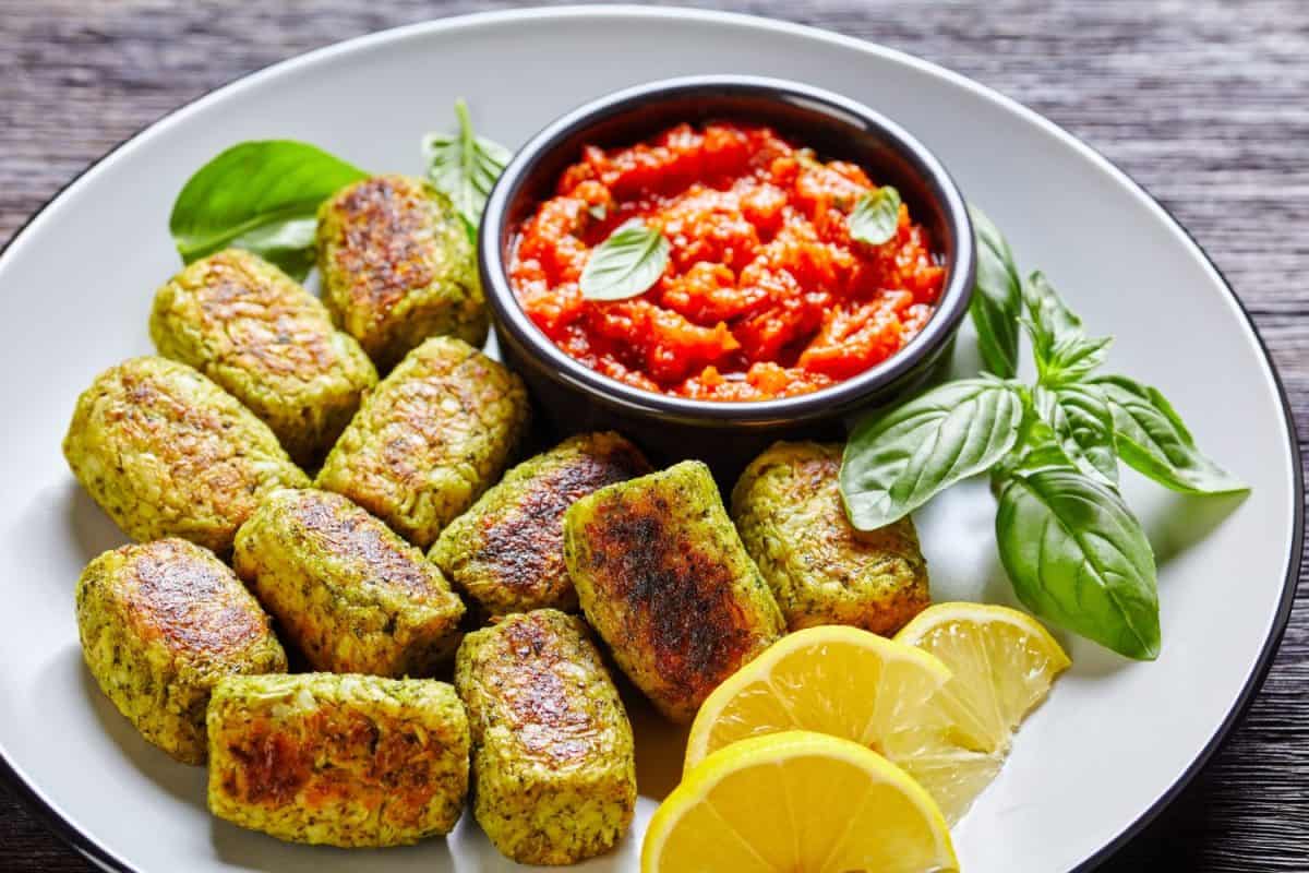 baked broccoli tots on a plate with marinara sauce on a dark wooden table, horizontal view from above, close-up