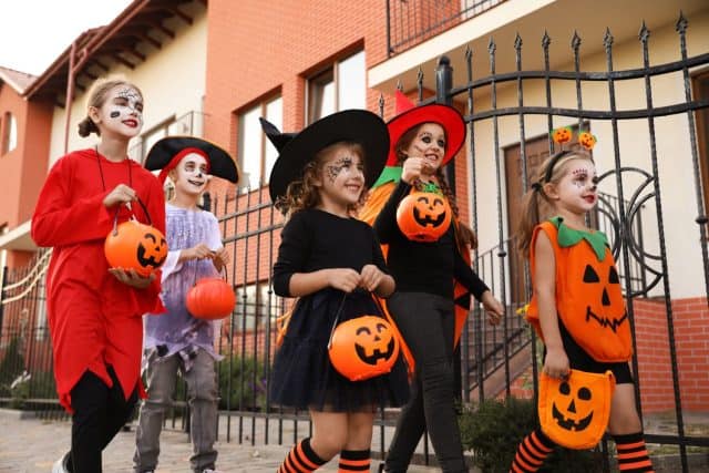 Cute little kids wearing Halloween costumes going trick-or-treating outdoors