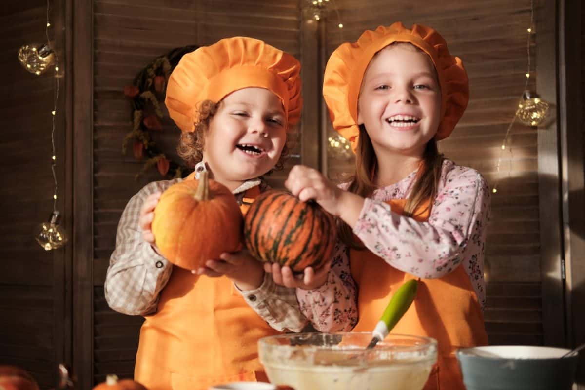 funny boy and girl in orange chef costumes prepare pumpkin pie. kids are getting ready for Thanksgiving. the concept of a family holiday