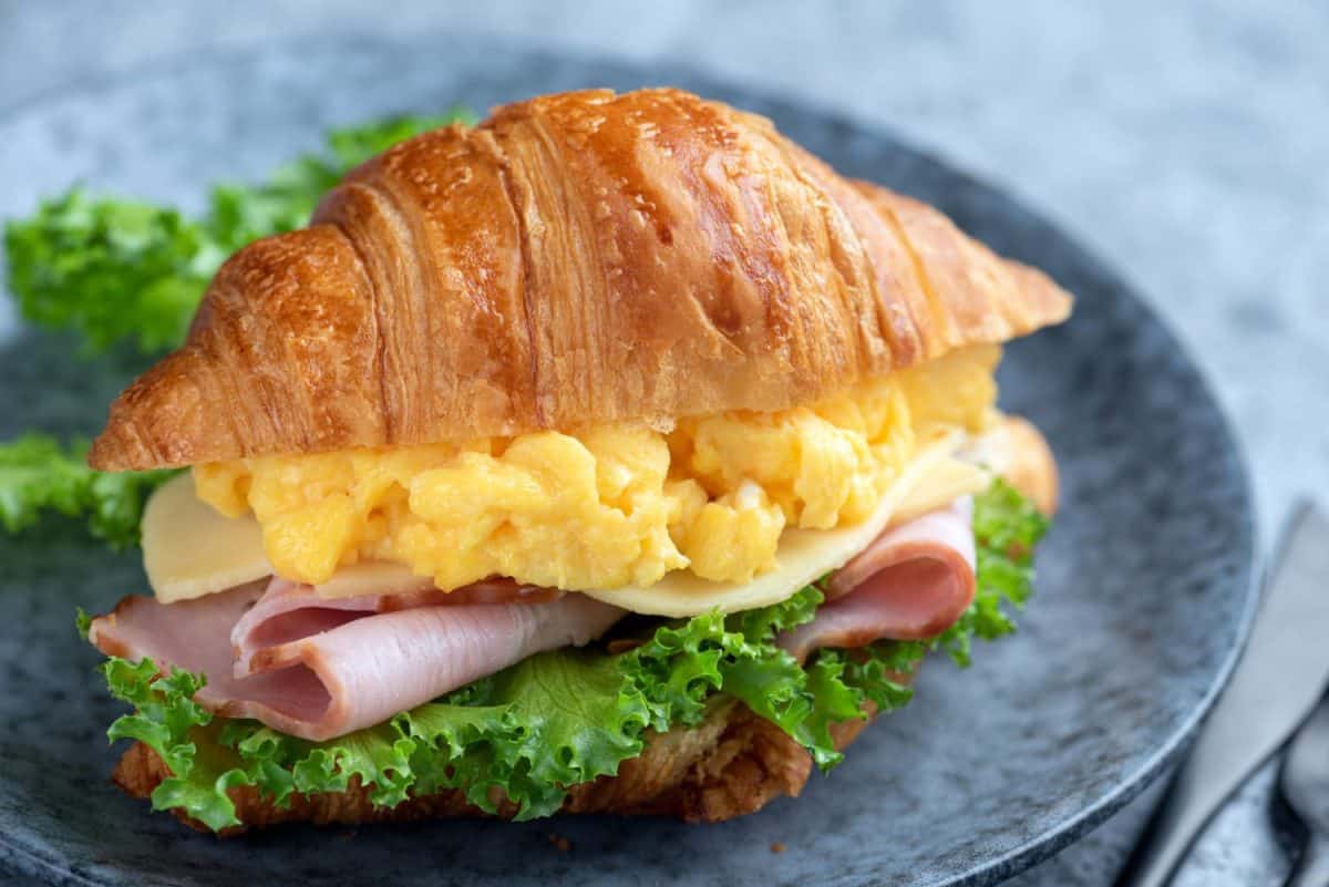 Croissant sandwich with egg and ham on a plate, closeup view. Tasty sandwich