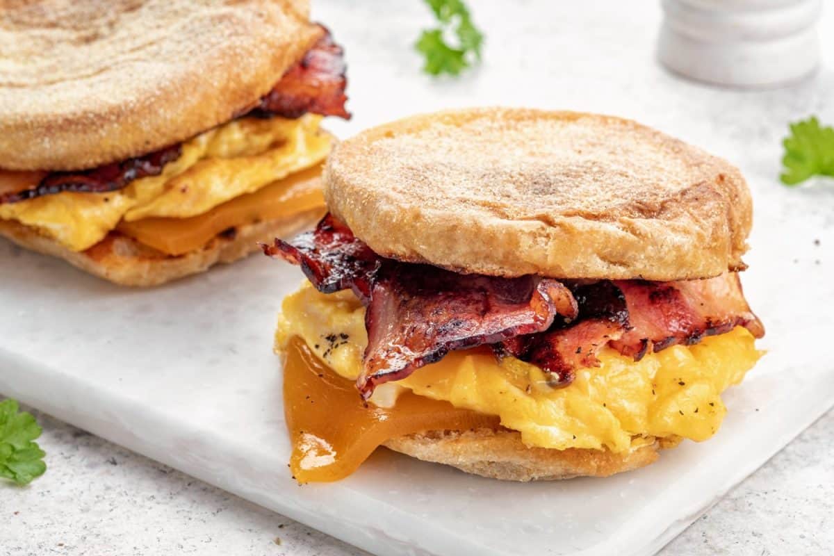 English muffin, scrumbled egg, ham, and cheese breakfast sandwich on a cutting board