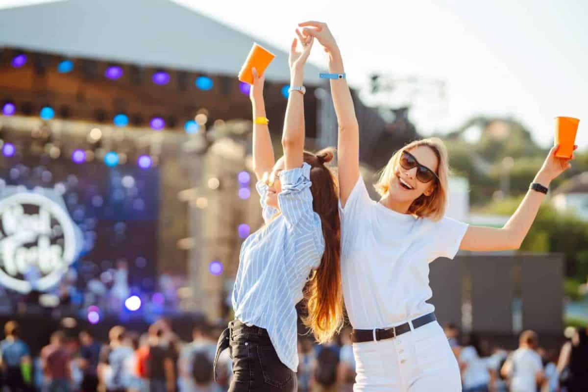 Two young woman drinking beer and having fun at Beach party together. Happy girlfriends having fun at music festival. Summer holiday, vacation concept.