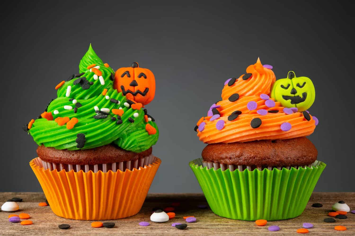 Cupcake on Halloween. Pumpkin Jack o lantern. Dessert on Halloween party. Muffin decorated with colored sprinkles, frosting and Icing shaped pumpkin Jack-o-lantern. Cupcakes on a wooden table.