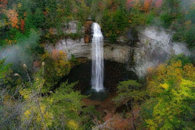 Photo of Falls Creek Falls in an autumn morning mist. Fall colors surround a ribbon of water falling from a rock cliff into a dark pool below. Taken at Falls Creek Falls State Park in Tennessee.