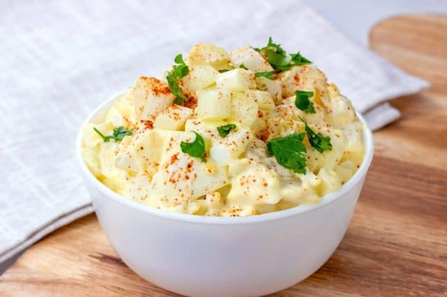 Fresh homemade traditional old-fashioned Amish Potato Salad with potatoes, boiled eggs, creamy dressing and celery in a white bowl on wooden background