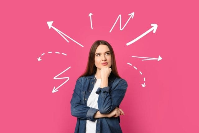 Choice in profession or other areas of life, concept. Making decision, thoughtful young woman surrounded by drawn arrows on pink background