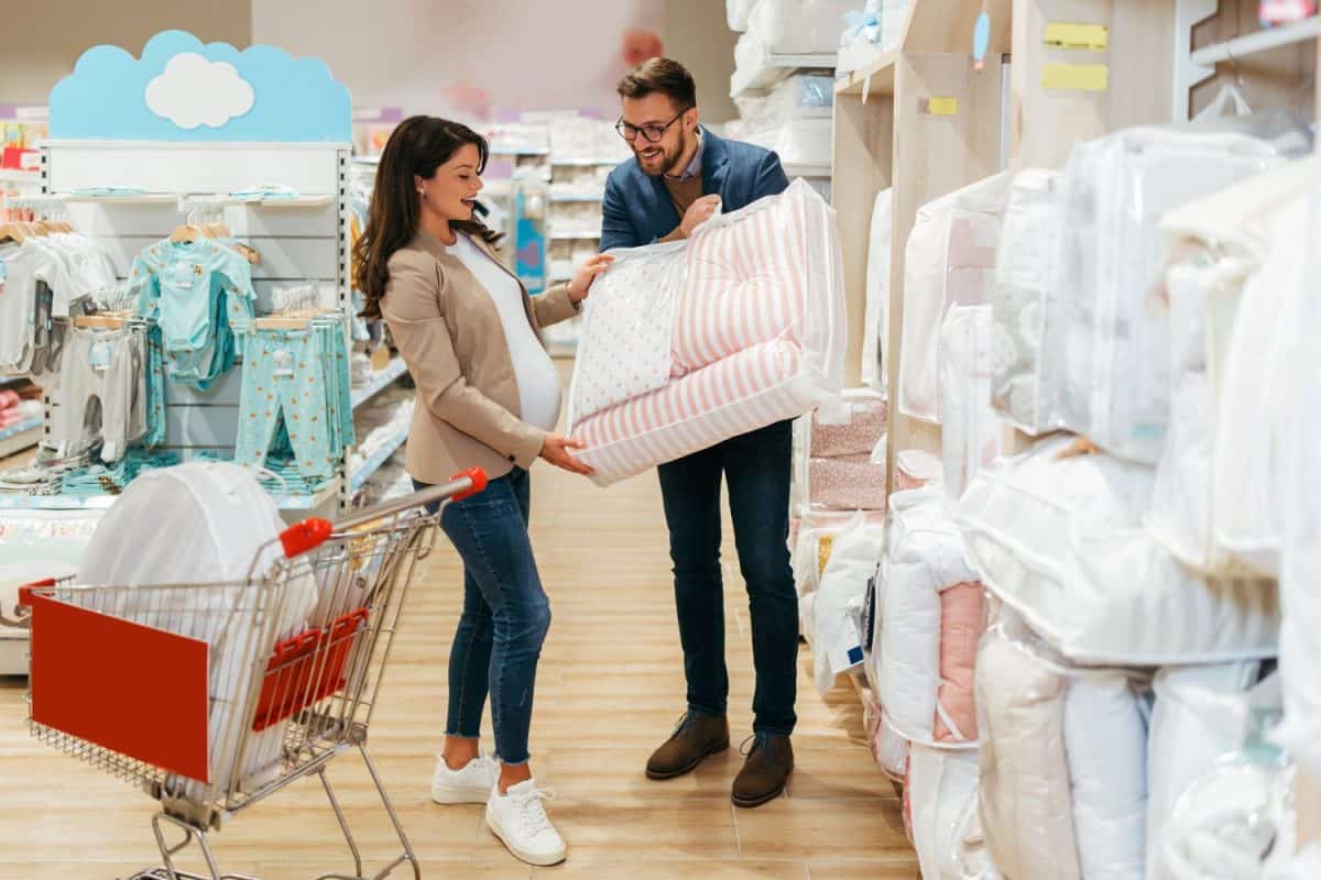 Attractive middle age couple enjoying in buying clothes and bed sheets for their new baby. Heterosexual couple in baby shop or store. Expecting baby concept.